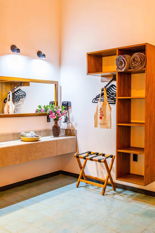 Cálido closet de madera y vanidad con lavamanos en habitación de huéspedes Casa Sofi Oaxaca, decorada con flores rosas y artesanías tejidas