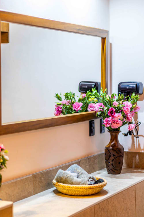Baño elegante en Casa Sofi Oaxaca con espejo de marco de madera, flores rosas y canasta tejida de amenidades