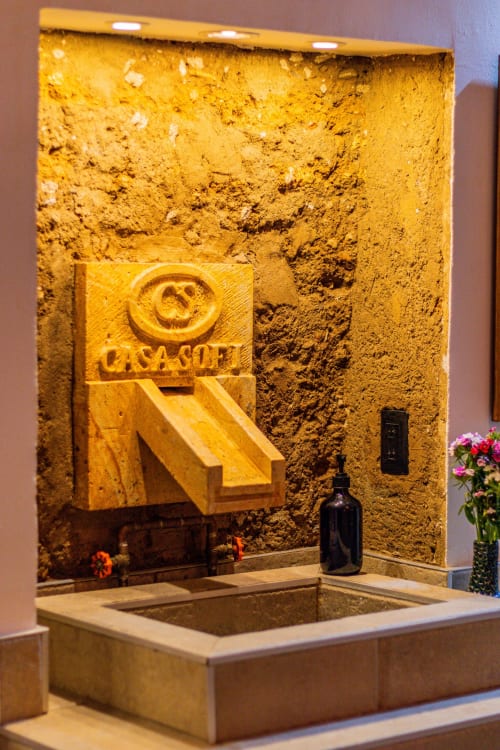 Fuente decorativa de Casa Sofi Oaxaca con muros de textura dorada y emblema del logo tallado