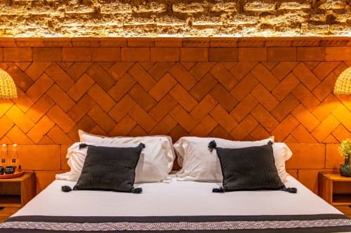 Dormitorio moderno en Casa Sofi Oaxaca con pared en espiga terracota, ropa blanca, almohadas negras e iluminación ambiental cálida.