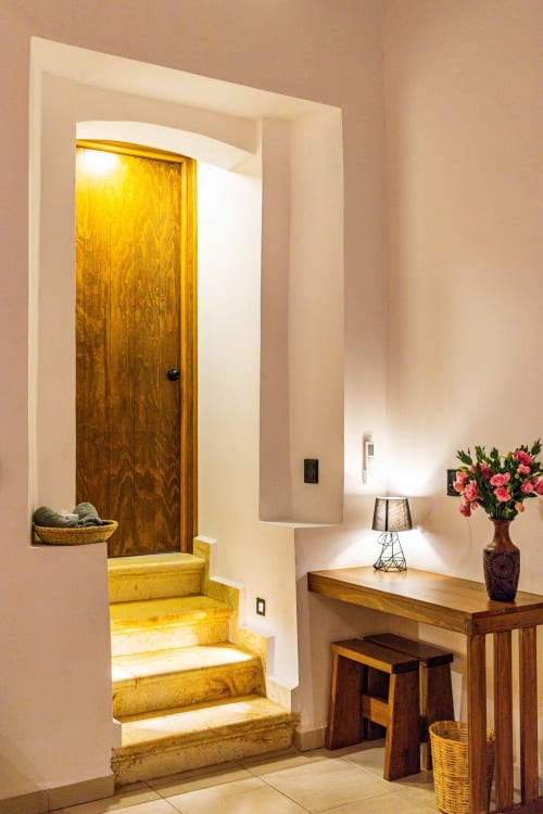 Entrada de Casa Sofi Oaxaca con puerta de madera, escalones amarillos, consola con flores y lámpara