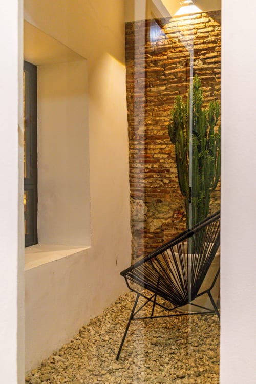 Patio moderno de Casa Sofi Oaxaca con silla de alambre negro, pared de ladrillo expuesto, planta de cactus y piso de grava