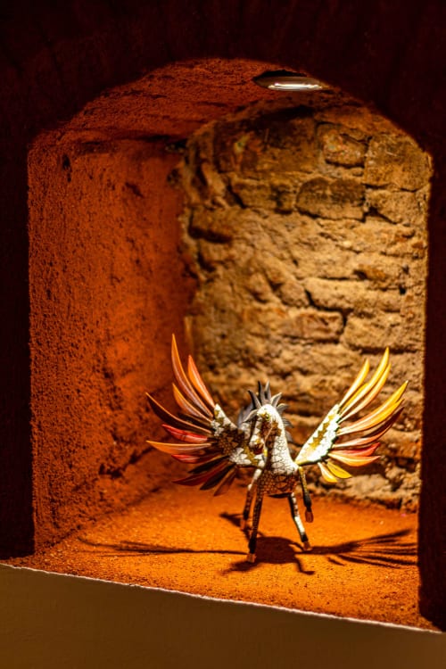 Escultura de pájaro ornamentada con plumas coloridas en el arco de terracota de Casa Sofi Oaxaca