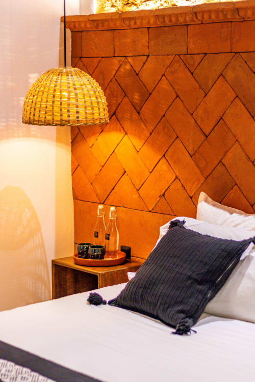 Acogedora habitación en Casa Sofi Oaxaca con lámpara de tejido, cabecero de ladrillo naranja y almohada oscura en ropa blanca