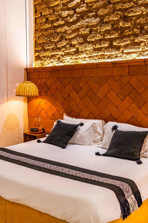 Moderna habitación en Casa Sofi Oaxaca con cabecera de ladrillo terracota, ropa de cama blanca, almohadas negras e iluminación cálida.
