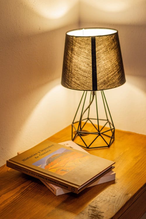 Lámpara de mesa moderna con base geométrica y pantalla texturizada junto a libros en Casa Sofi Oaxaca