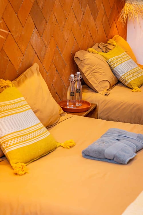 Acogedora habitación en Oaxaca con almohadas amarillo dorado, muros de ladrillo, botellas de agua y toallas dobladas en Casa Sofi