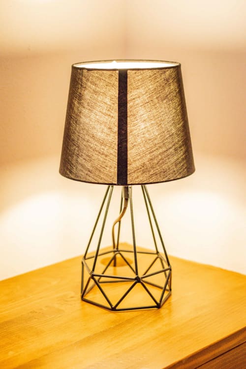 Lámpara de mesa moderna con base geométrica de latón y pantalla texturizada en oro sobre superficie de madera en la boutique Casa Sofi Oaxaca