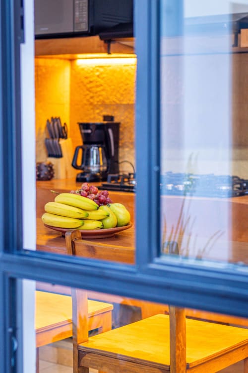 Ventana de cocina con marco azul en la cabaña Casa Sofi Oaxaca mostrando plátanos y uvas sobre mesa de madera