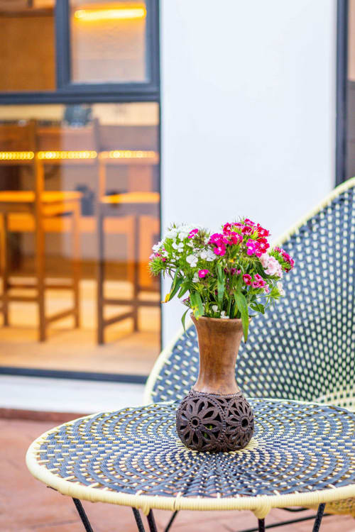 Flores rosas y blancas en florero decorativo sobre mesa de patio en Casa Sofi Oaxaca, con escaparate iluminado visible