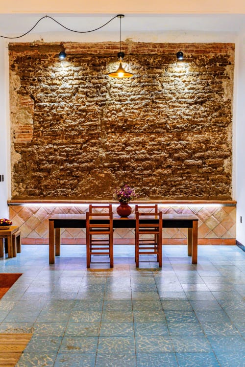 Comedor de la Casa Sofi Oaxaca con muro de piedra rústica, mesa de madera, sillas y lámparas colgantes