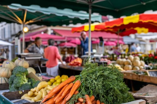 Lebendiger Wochenmarkt in Epinac mit frischem Gemüse, Karotten und farbenfrohen Schirmen