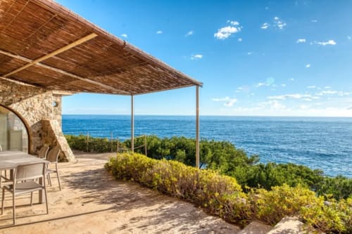 Terrasse méditerranéenne avec bâtisse en pierre, structure ombragée en bois dominant la mer bleue et la verdure à Palafrugell