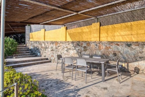 Espace de restauration extérieure à l'hôtel Finques Garcia Enrich à Palafrugell avec murs en pierre, voiles d'ombrage jaunes et mobilier moderne.