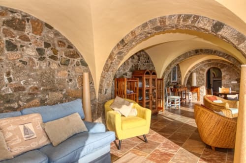 Couloir voûté en pierre avec canapé bleu et chaise jaune à Finques Garcia Enrich, Palafrugell