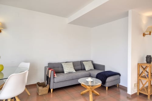 Sala d'estar moderna de l'hotel Finques Garcia Enrich a Palafrugell amb sofà gris, taula rodona de fusta i disseny contemporani