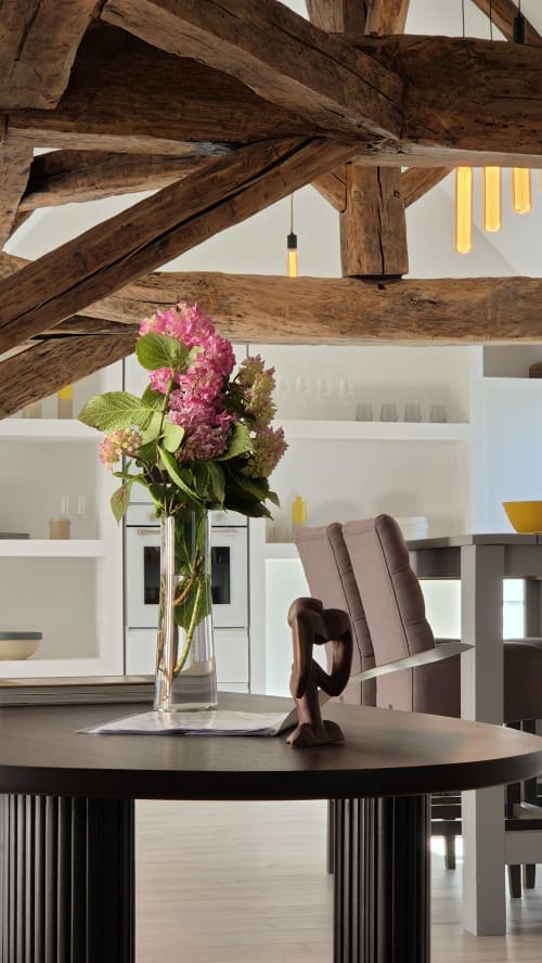 Modern eetgedeelte in Moulin Renaudiots met blootgestelde houten balken, ronde tafel, roze hortensia's en stadsuitzicht