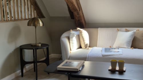 Gezellige zithoek in Moulin Renaudiots met crèmekleurige bank, zwart bijzettafeltje, koperen lamp en blootgestelde houten balken