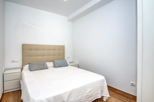 Dormitori modern a Finques Garcia Enrich, Palafrugell amb capçal beige, roba de llit blanca i sòl de fusta