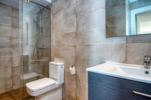 Bany modern de l'hotel Finques Garcia Enrich a Palafrugell amb dutxa a ras de sòl, WC blanc i lavabo blau.