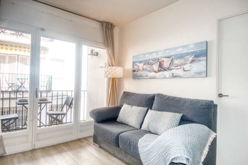 Bright living room with gray sofa, coastal artwork, and balcony overlooking Palafrugell at Finques Garcia Enrich