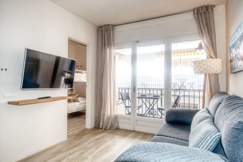 Modern hotel room at Finques Garcia Enrich in Palafrugell with blue sofa, wall-mounted TV, and balcony overlooking the town