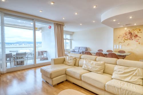 Lujosa sala de estar con sofá seccional de cuero crema, balcón con vistas al mar y mobiliario moderno en Palafrugell