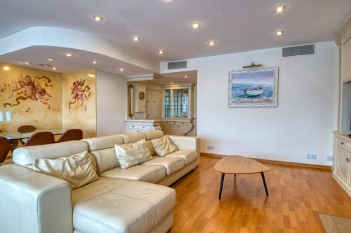 Elegante sala de estar en Finques Garcia Enrich en Palafrugell con sofá de cuero crema, suelo de madera e iluminación moderna