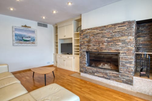 Salón moderno con chimenea de piedra, carpintería integrada y pisos de madera en Finques Garcia Enrich en Palafrugell
