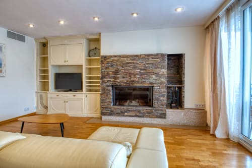 Salón moderno con mobiliario color crema, chimenea de piedra y suelos de madera en Finques Garcia Enrich en Palafrugell