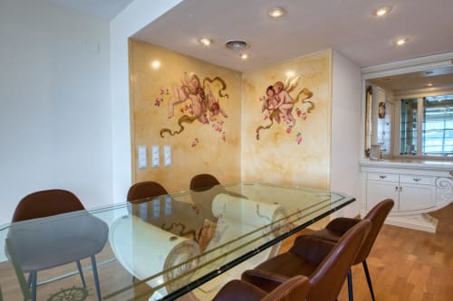 Comedor moderno en Finques Garcia Enrich, Palafrugell, con mesa de cristal, murales de querubines y mobiliario elegante
