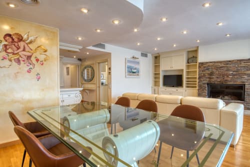 Elegante salón en Finques Garcia Enrich, Palafrugell con mesa de comedor de cristal, sofá color crema, chimenea y muebles empotrados