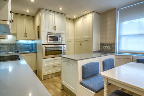 Cocina moderna con gabinetes color crema, electrodomésticos de acero inoxidable y barra de desayuno tapizada en azul en Finques Garcia