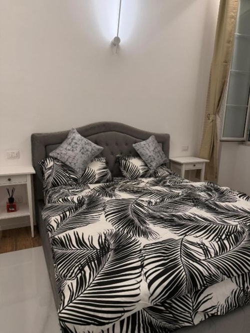 Letto imbottito grigio con biancheria a motivi foglie bianche e nere, cuscini grigi nella camera Roma di St Mary Major Loft