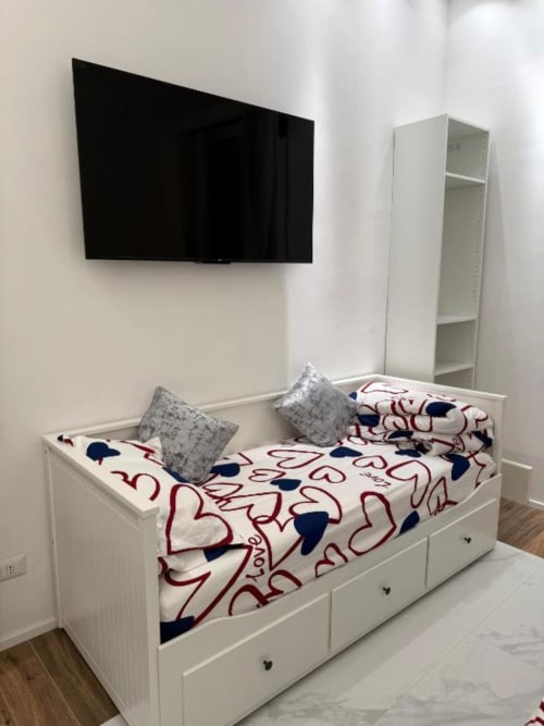 Camera da letto moderna al St Mary Major Loft Roma con letto bianco, biancheria a motivi, TV a parete e libreria