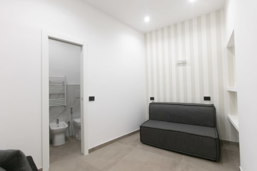 Suite Modern Gold di Pignasecca Domus Napoli con divano letto scuro, carta da parati a righe e bagno in camera