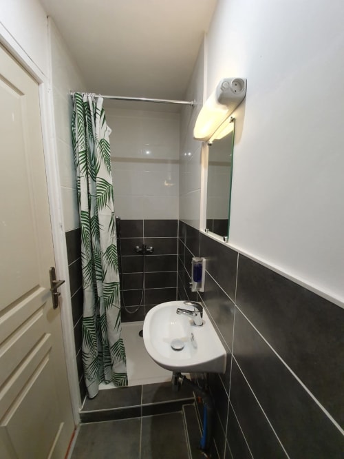 Salle de bain moderne du gîte NancyRoom avec carrelage noir et blanc, lavabo blanc, miroir de vanité et rideau de douche tropical