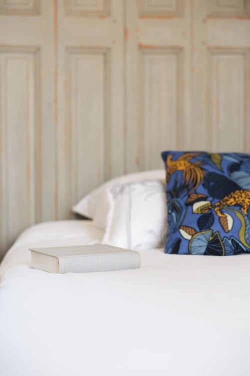 Lit douillet à La Maison D'olivier avec oreillers blancs, coussin bleu patterné et livre à Mesnard-la-Barotière