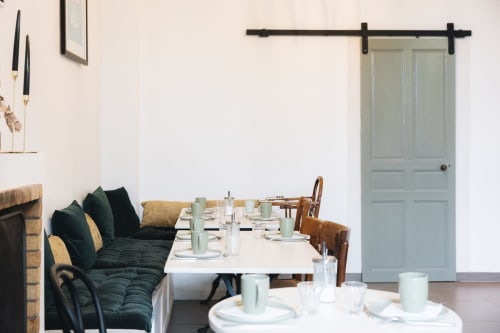 Salle à manger de la Maison d'Olivier avec banquette, table blanche et porte grange sage à Mesnard-la-Barotière