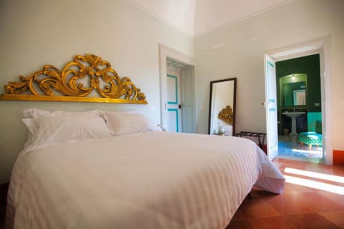 Camera da letto luminosa a Villa Ceci ad Andria con letto bianco, testata dorata ornamentale, pavimenti in terracotta e vista sul giardino