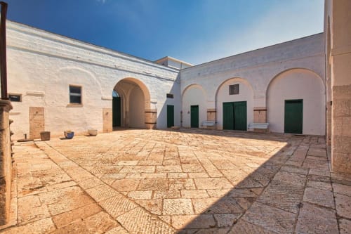 Il soleggiato cortile di Villa Ceci ad Andria con muri imbiancati, porte verdi e pavimentazione in pietra geometrica