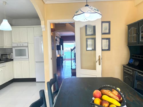 Área de cocina-comedor del apartamento dúplex Xanela en Baiona con vistas al mar, muebles color crema, mesa negra y frutero