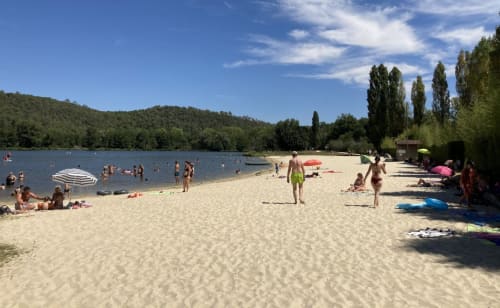 Sandy beach with swimmers at Domaine De Campagnac in Carsac-Aillac, France, featuring calm waters and forested hills