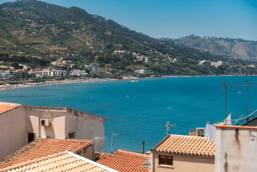 CefalHome overlooks turquoise Mediterranean waters, beach, and hillside village near Roma