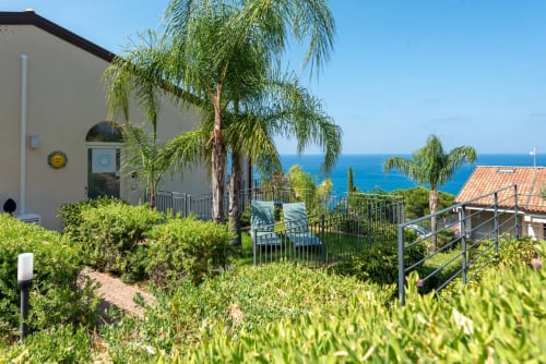 CefalHome Mediterranean villa with sea views, palm tree, and coastal garden overlooking blue ocean from Rome property