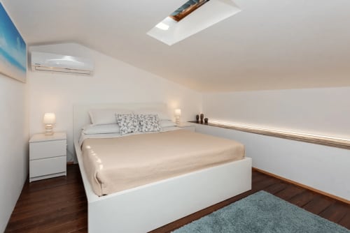 Modern bedroom in CefalHome Roma with white bed, skylight, air conditioning, and wooden flooring
