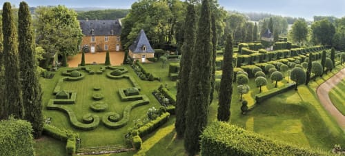 Aerial view of Domaine De Campagnac's manicured French gardens with cypress trees, ornate hedges, and stone manor house in