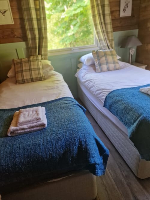 Twin beds with blue blankets and tartan pillows in a cottage bedroom with garden views at Grouse Lodge, Dunoon