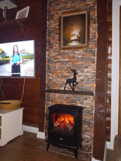Cozy cottage living room with stone fireplace, electric stove, and TV at Grouse Lodge in Dunoon