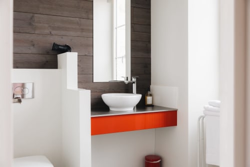 Lavabo moderne blanc avec tiroirs rouges à La Maison D'olivier B&B, mur d'accent en bois foncé